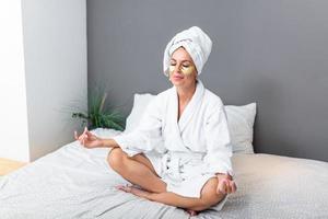 Woman sitting on bed and meditates. Woman sitting on bed and working yoga exercise. Young woman meditating . Pretty girl sitting in bed in the morning. Beautiful young woman doing yoga photo