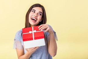 Portrait of nice girlish childish winsome attractive cheerful lady wearing striped pullover holding in hand opening large red gift box guessing isolated on bright vivid yellow background photo