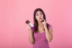 Teenage girl with acne problem holding chocolate bar against pink background. Young beautiful Woman Acne Problem Face with Chocolate bar UnHappy Eating,His Stressful face. photo