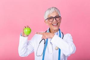 Smiling mature nutritionist holding a fruit and showing healthy juicy apple. Doctor or nutritionist hold an apple. Good medical healthcare nutrition concept. An apple a day keeps the doctor away photo