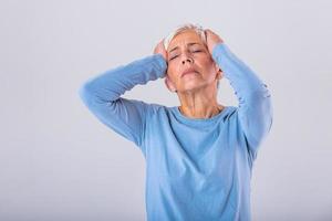 Mature woman holding her head with her hands while having a headache and feeling unwell. Senior woman with headache, pain face expression. Elderly woman having head pain migraine photo