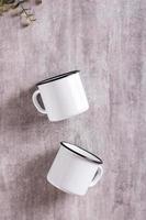 Two white empty metal mugs on a gray background in a vertical view. Top view photo