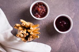 Closeup of crispy sweet straws with berry filling and two bowls of jam in a container. Top view. photo