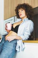 adulto mujer con desabrochado camisa Bebiendo café en cocina foto