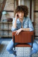 Smiling woman in denim jacket and jeans sitting on chair photo