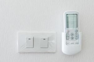remote Control of the air conditioner and light switch on  the white wall photo