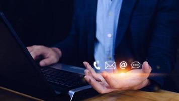 Contact us or Customer support hotline people connect. Businessman using showing and touching on virtual screen contact icons call phone, email, address, live chat, photo