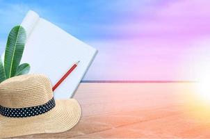 Notebook with pencil and straw hat on sea and sand of a beach nature landscape background photo