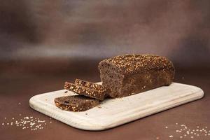 Black Bread with Cereals sliced on a wooden cutting board against a Brown Background. Preparing the Dinner Table photo