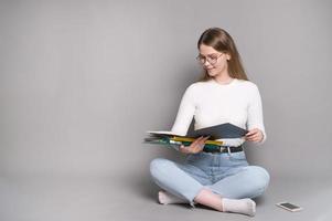 A cute student with glasses is sitting on a gray background and looking at folders for documents photo
