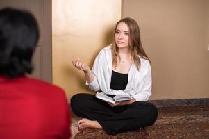 A nice girl psychologist is receiving a client sitting on the floor with a diary photo