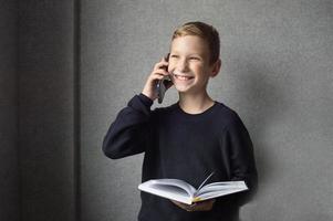A happy boy is holding a book in his hands and talking on the phone photo