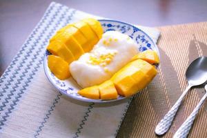 Mango sticky rice topped with coconut milk and soybeans placed in a traditional Chinese style dish on a wooden table. photo