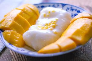 Mango sticky rice topped with coconut milk and soybeans placed in a traditional Chinese style dish on a wooden table. photo