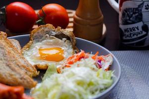 Breakfast, fried eggs, fried sausage, vegetable salad and toast on a brown wooden table with coffee. photo