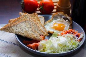 Breakfast, fried eggs, fried sausage, vegetable salad and toast on a brown wooden table with coffee. photo