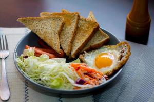 Breakfast, fried eggs, fried sausage, vegetable salad and toast on a brown wooden table with coffee. photo