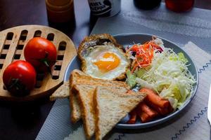 Breakfast, fried eggs, fried sausage, vegetable salad and toast on a brown wooden table with coffee. photo