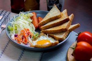 Breakfast, fried eggs, fried sausage, vegetable salad and toast on a brown wooden table with coffee. photo