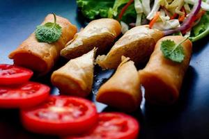 Fried spring rolls with vegetables and tomatoes placed in a black plate on a black wooden table and dipping sauce. photo