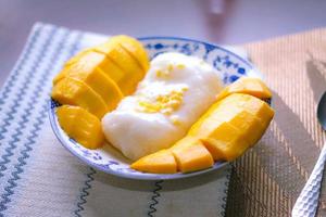 Mango sticky rice topped with coconut milk and soybeans placed in a traditional Chinese style dish on a wooden table. photo