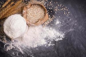 Flour and wheat grains in sacks with wheat ears On a black background table. In a rustic kitchen. Top view. photo