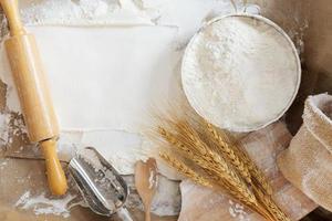 Flour in a bowl and wheat grains with wheat ears on the table, paper background In a rustic kitchen, top view photo