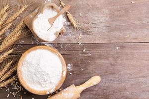 wheat flour in a wooden bowl There are ears of wheat on the table. Old wooden background - top view photo