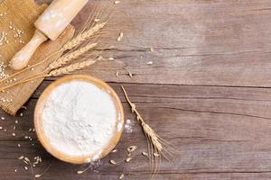 wheat flour in a wooden bowl There are ears of wheat on the table. Old wooden background - top view photo