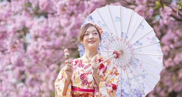 Japanese woman in traditional kimono dress holding umbrella and sweet hanami dango dessert while walking in the park at cherry blossom tree during spring sakura festival with copy space photo