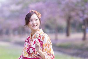 japonés mujer en tradicional kimono vestir participación dulce hanami dango postre mientras caminando en el parque a Cereza florecer árbol durante primavera sakura festival con Copiar espacio foto