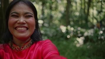 Portrait of a beautiful Asian woman in a red blouse taking a selfie inside the rainforest video