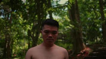 retrato de un joven asiático hombre con un desnudo cofre caminando solitario mientras mirando a el cámara en el bosque video