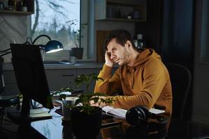 el hombre cansado trabaja hasta tarde en el lugar de trabajo por la noche foto