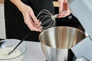 Woman put in whisk nozzle in electric mixer photo