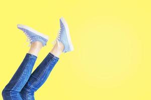 Female legs in jeans and sneakers in pose on yellow background photo