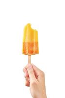 Paleta de helado de fruta congelada amarilla mordida en mano de mujer sobre fondo blanco foto