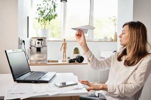 Woman plays with paper plain at home office. Procrastinate at remote work photo