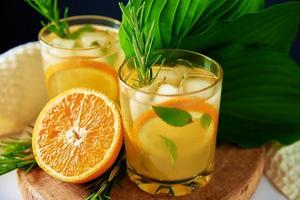 Orange fresh lemonade with rosemary in glass on table photo