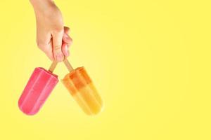 Two color popsicles in woman hands on yellow background photo