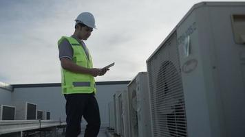 Asian maintenance engineer works on the roof of factory. contractor inspect compressor system and plans installation of air condition systems in construction. technology, online checking video