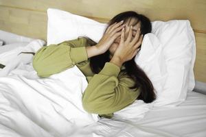 un triste joven asiático mujer es llorando mientras acostado en el cama foto