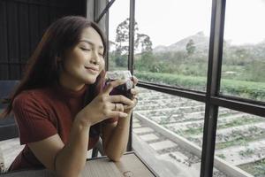 Portrait of joyful young woman enjoying a cup of tea at home. Smiling pretty girl drinking telang tea in rainy season. photo