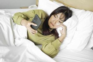 un triste joven asiático mujer es llorando terminado su teléfono mientras acostado en el cama foto