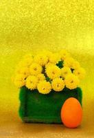 Painted eggs with grass pedestal with yellow chrysanthemums on shiny background. Easter. Copy space photo