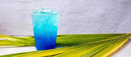 bebida hawaiana azul en un vaso de plástico y hojas de coco. foto