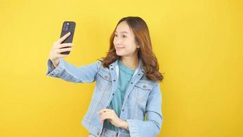 Smiling Asian woman looking at device holding camera taking selfie and video chatting online