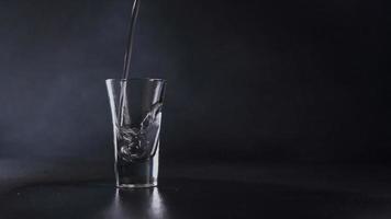 ein Strom von Wasser gießt in ein Glas gegen ein grau Hintergrund. Wasser Spritzen. schließen oben video