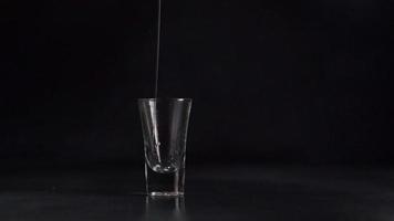 A Stream of Water pours into a Glass against a black background. Water splash. Slow-motion. 120fps video