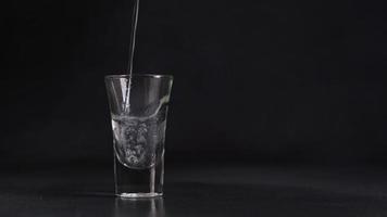 un corriente de agua vierte dentro un vaso en contra un negro antecedentes. agua chapoteo. cerca arriba video
